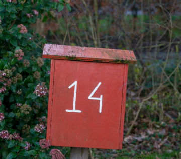 A red mailbox sitting next to a bush